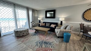 A living room with a sofa, a coffee table, a patterned rug, and a view through a window with curtains.