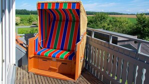 A wicker chair with a striped cushion on a wooden deck with a white picket fence. - Apartment Haffblick - Beautiful holiday apartment for up to 4 people. (Insel Poel / OT Kaltenhof)