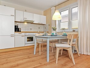 Une cuisine moderne avec des meubles blancs, un four encastré et un coin repas comprenant une table et des chaises.