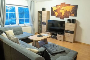 Ein modernes Wohnzimmer mit einem grauen Sofa, einem Holztisch, einem Fernseher und einer Kommode mit Schubladen.