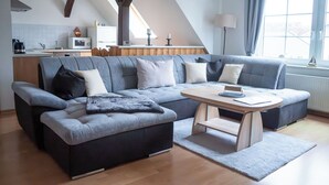 A modern living room with a sectional sofa, a wooden coffee table, and a kitchen in the background. - Apt. WINDROSE - Cozy semi-detached house for 4 people (Insel Poel / OT Gollwitz)