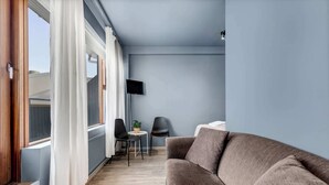 Een kamer met een bruine bank, een televisie aan de muur en een kleine tafel met stoelen.