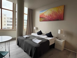 Une chambre dâhĂŽtel avec un lit, des tables de chevet, un bureau et une fenĂȘtre donnant sur des immeubles.