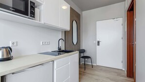 Een kleine keuken met een magnetron, waterkoker, spoelbak en een kleine stoel.