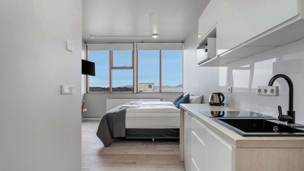 Een moderne slaapkamer met een bed, nachtkastje en uitzicht op het omliggende landschap door grote ramen.