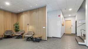 A reception area with a modern design, featuring a reception desk, three armchairs, a small round table, and a vertical wooden panel wall. - Iceland Comfort Apartments Economy Studio (Kópavogur)