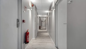 A long, narrow hallway with white walls, a fire extinguisher mounted on the left wall, and a door at the end. - Iceland Comfort Apartments Economy Studio (Kópavogur)