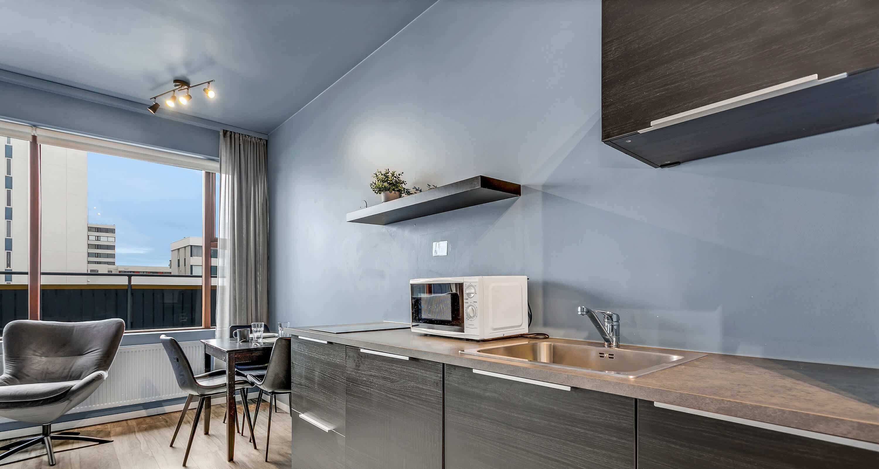 A modern kitchen with a built-in microwave, stainless steel sink, and a small potted plant on a floating shelf.