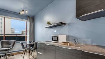 A modern kitchen with a built-in microwave, stainless steel sink, and a small potted plant on a floating shelf.