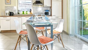 A modern kitchen with white cabinets, a stainless steel range hood, and a dining area with a glass table and white chairs.