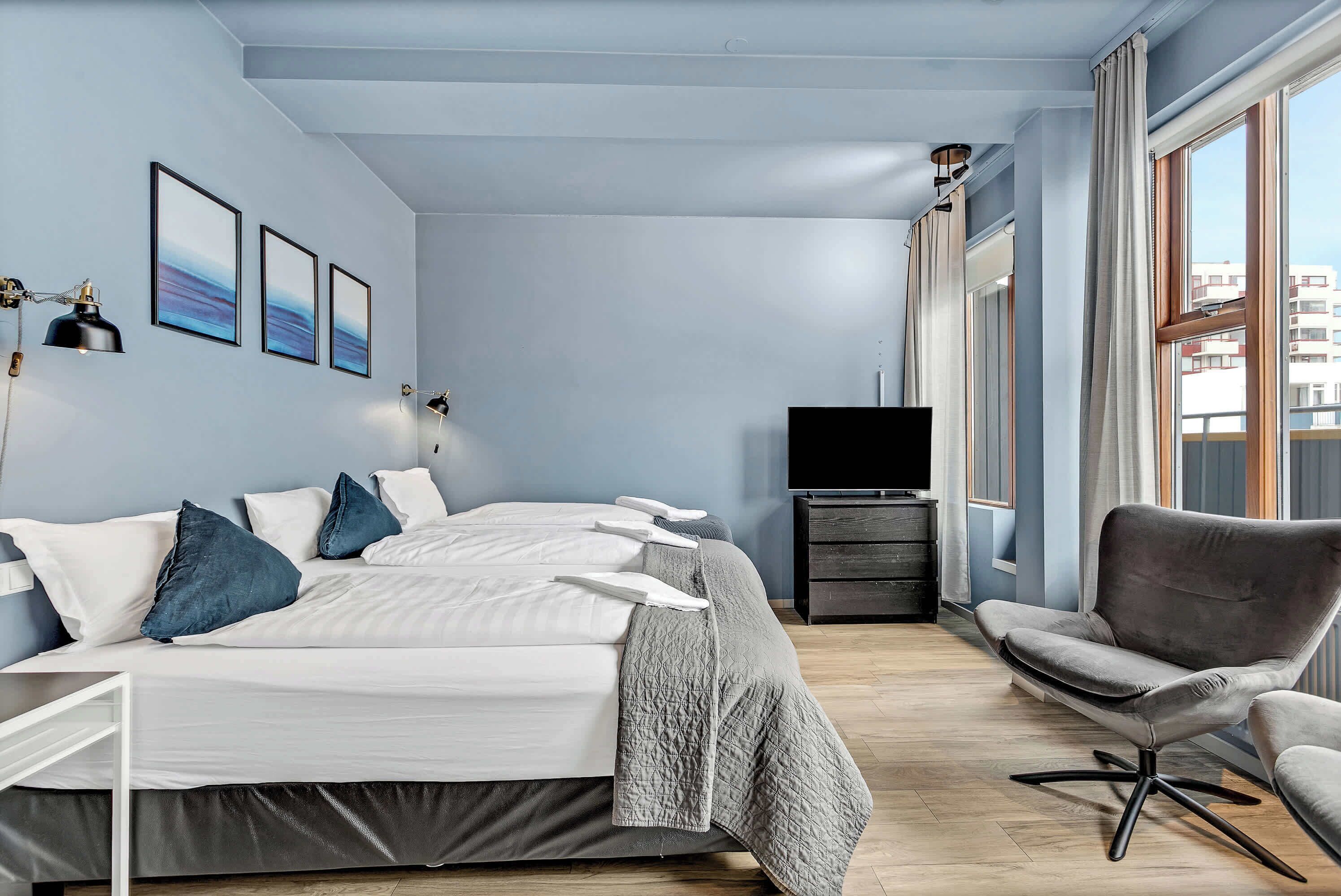 Une chambre d’hôtel avec un lit, une chaise, une télévision et une fenêtre avec des rideaux.
