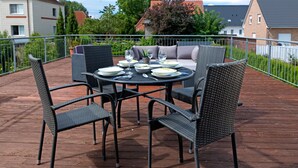 Een buiten eethoek met een ronde tafel en vier stoelen, omringd door een houten terras en een metalen balustrade.