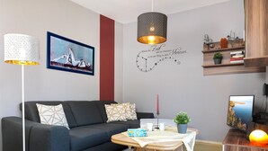 Un saló modern amb un sofà gris fosc, una taula de centre de fusta, un rellotge de paret i una estantàcia amb objectes decoratius.