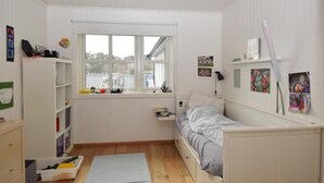 Una habitación pequeña y bien iluminada con una cama individual, una ventana y un estante con varios objetos.