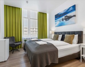A hotel room with a bed, a desk, a chair, and a painting on the wall.