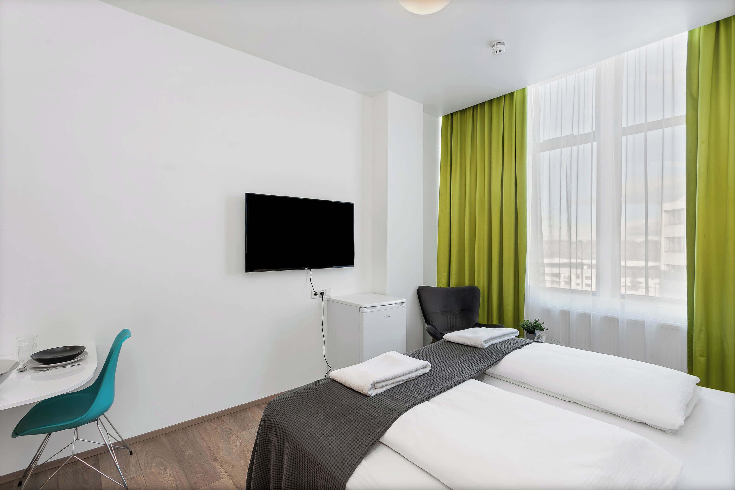 A hotel room with a bed, a desk, a chair, a TV, and a window with curtains.