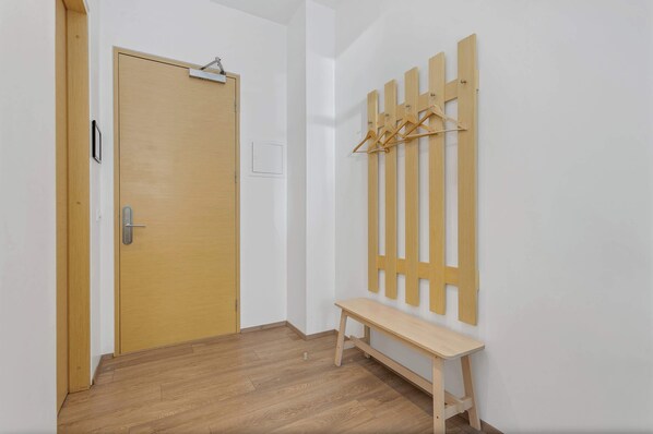 A hallway with a wooden door, a bench, and a wall-mounted wooden rack with hangers.