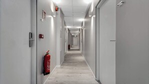 Un passadís llarg i estret amb parets blanques, un extintor fixat a la paret esquerra i una porta al final.