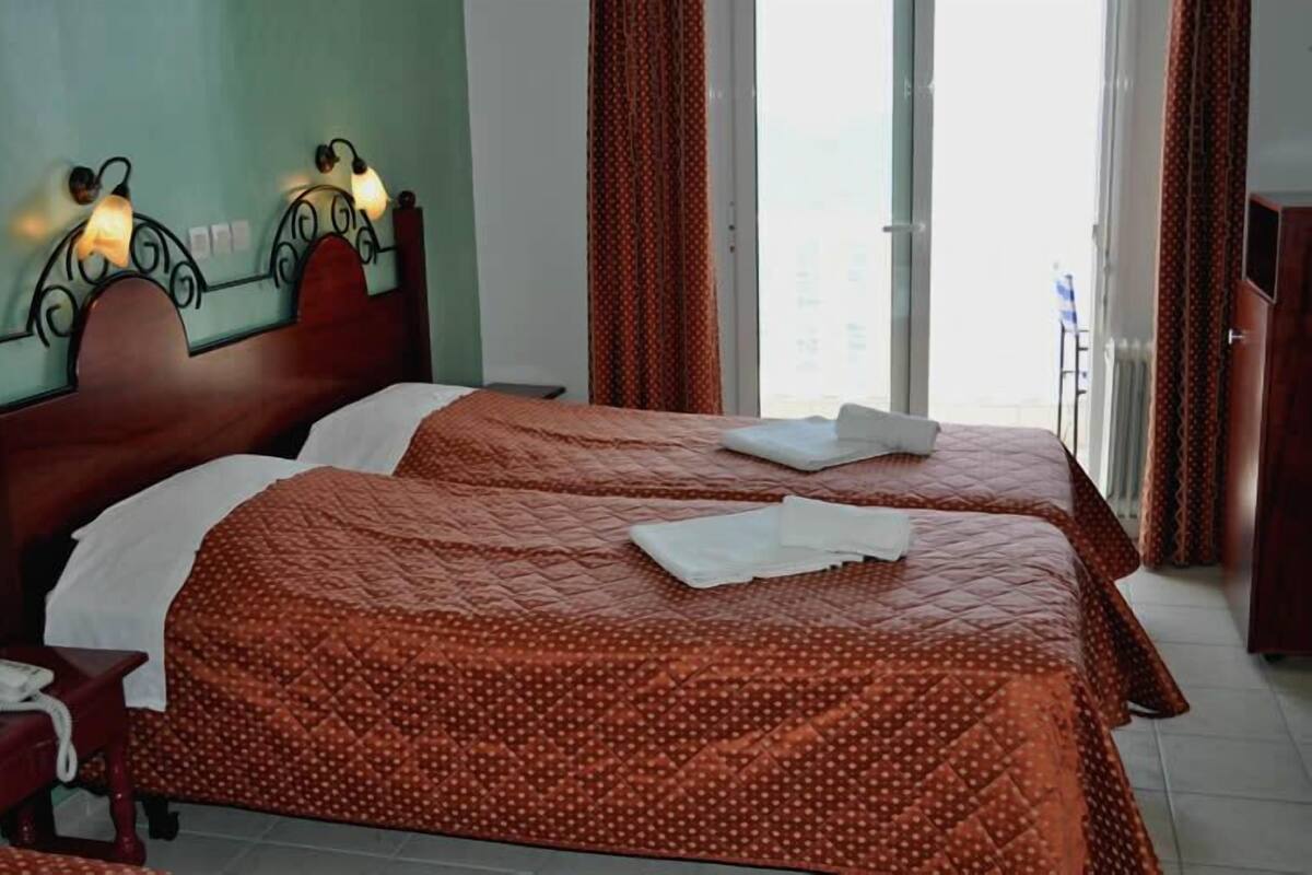 A hotel room with two beds, a wooden headboard, a telephone, and a view of the city through large windows.