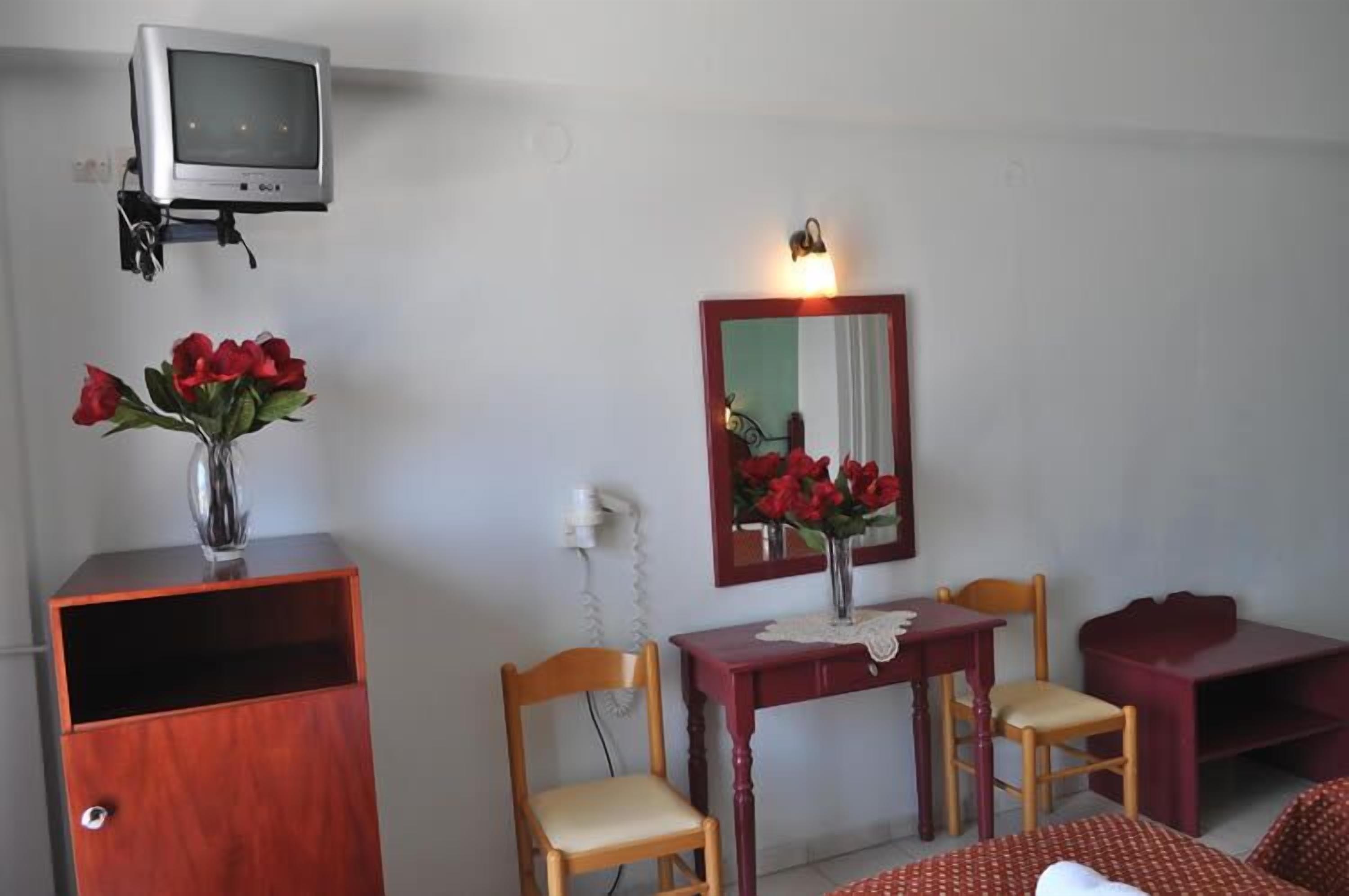 Una habitació amb un armari de fusta, una taula petita amb caires, un mirall i una televisió sobre un suport.