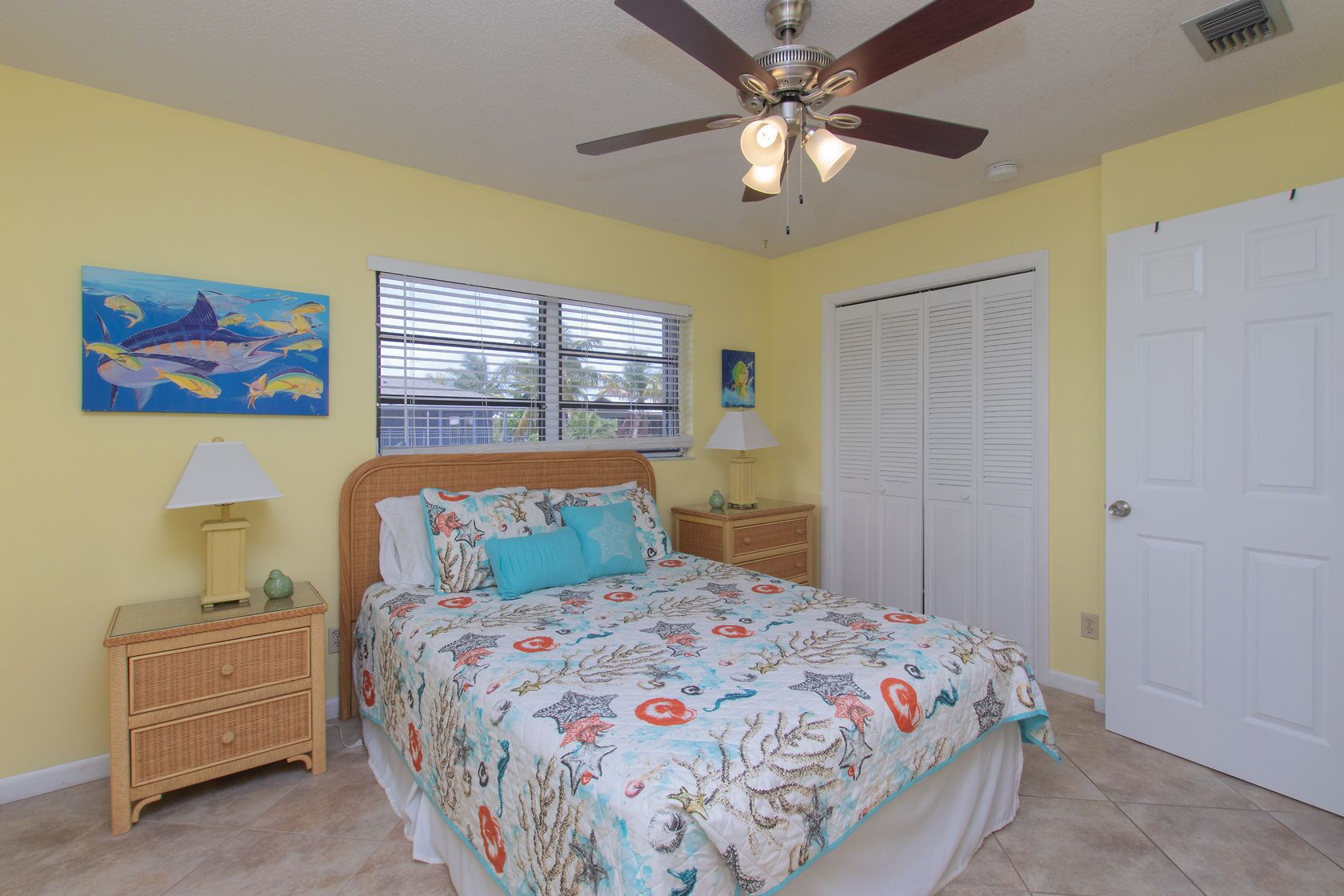 A bedroom with a bed, two nightstands, a ceiling fan, a window with blinds, a door, and a wall with a painting.