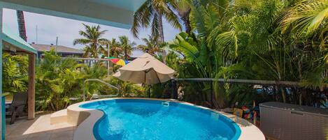 A hot tub surrounded by palm trees and a covered area with chairs.