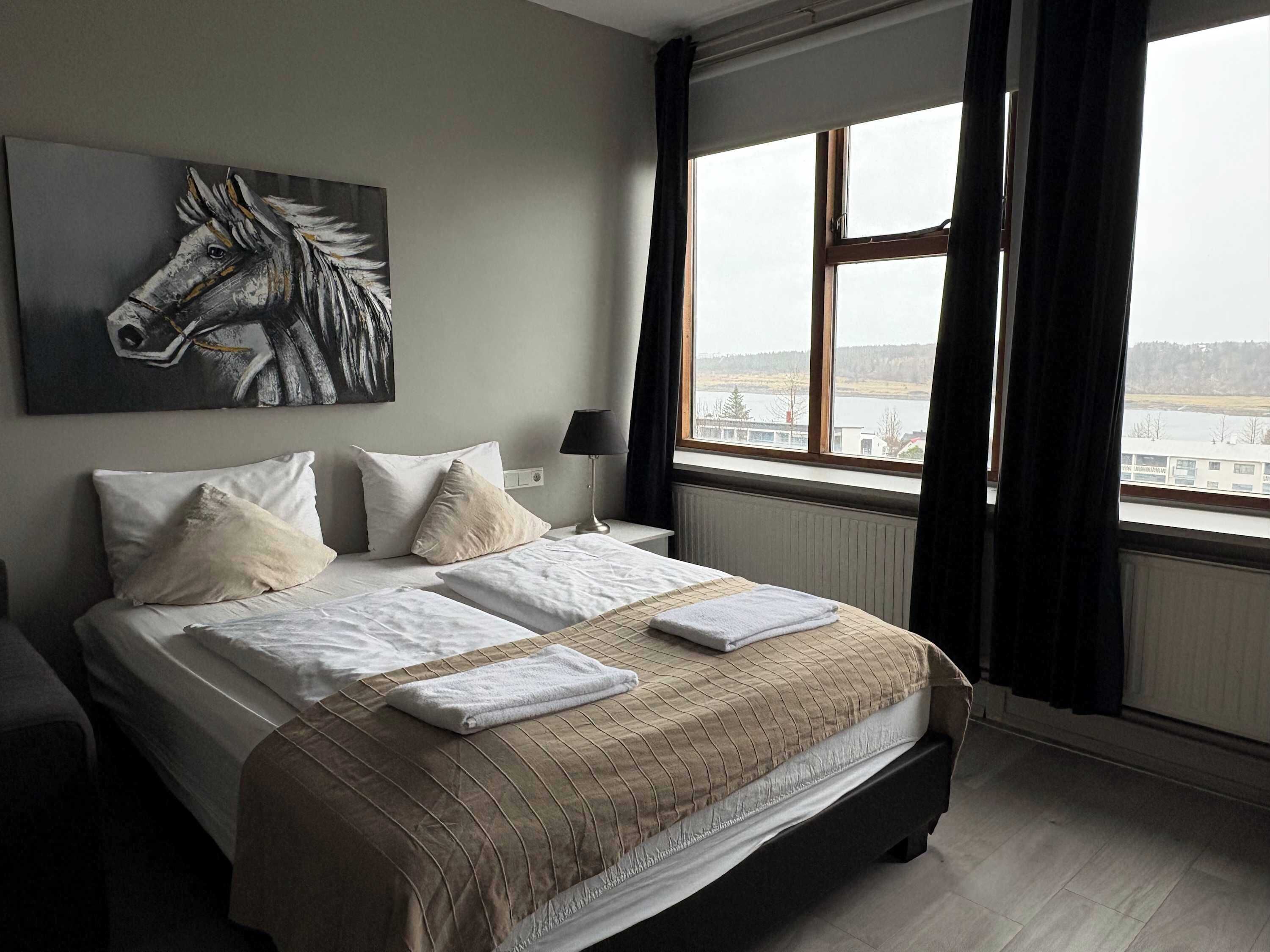 A hotel room with a bed, a window with a view, and a painting on the wall.