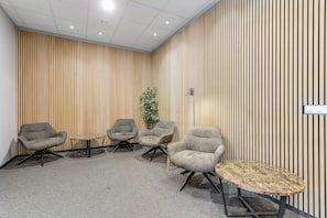 Uma sala de conferências com quatro cadeiras cinzentas, uma pequena mesa redonda e um painel de parede de madeira.