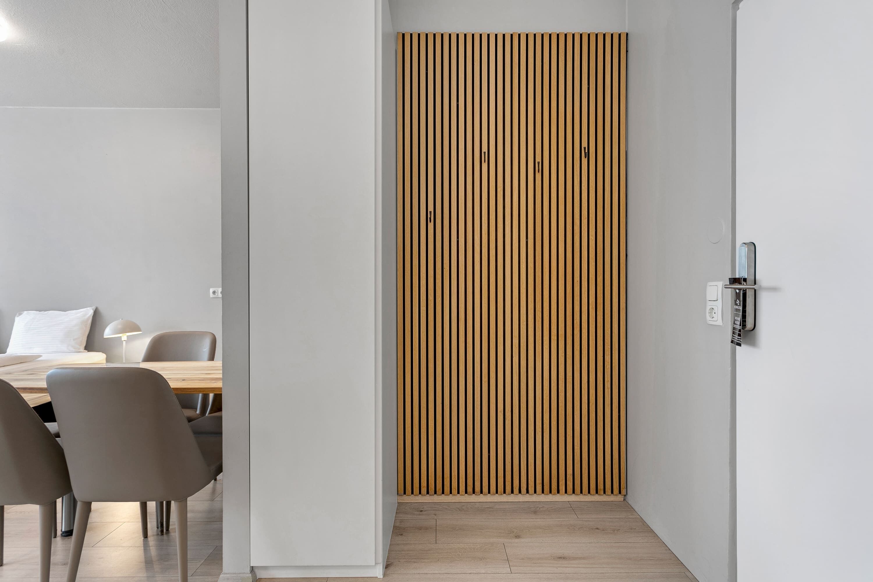 Een modern interieur met een wand van houten latten, een eethoek met stoelen en een tafel, en een lichtschakelaar op de muur.