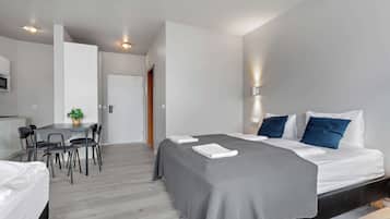 Een moderne hotelkamer met een bed, nachtkastjes, een bureau met stoelen, een potplant en een deur.