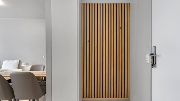 A modern interior with a wooden slat wall, a dining area with chairs and a table, and a light switch on the wall. - Iceland Comfort Apartments Studio for 5 (Kópavogur)