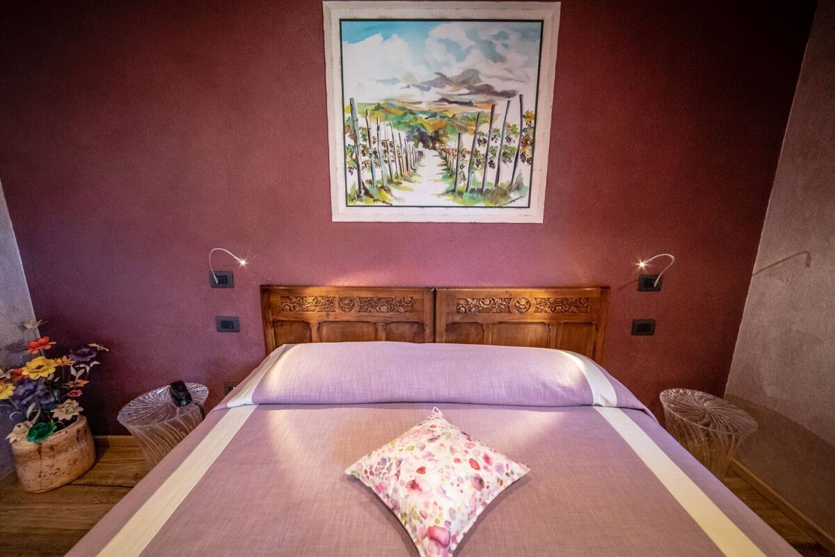 Ein Schlafzimmer mit einem Holz-Kopfteil, einem Bett mit einem floralen Kissen, einem Landschaftsbild an der Wand und zwei Wandlampen.