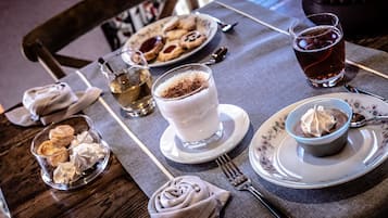 Un tavolo da pranzo con un piatto di biscotti, un bicchiere di tè freddo, un bicchiere di latte con panna montata, una ciotola di panna montata e un tovagliolo con un motivo a rosa.