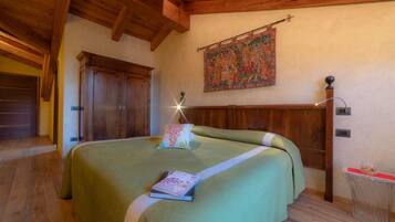 A bedroom with a large bed, wooden headboard, a tapestry on the wall, and a small table with a lamp.