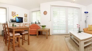 A living room with a wooden dining table, orange sofa, and a TV.