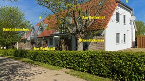 A two-story building with a red-tiled roof, surrounded by greenery and a hedge.