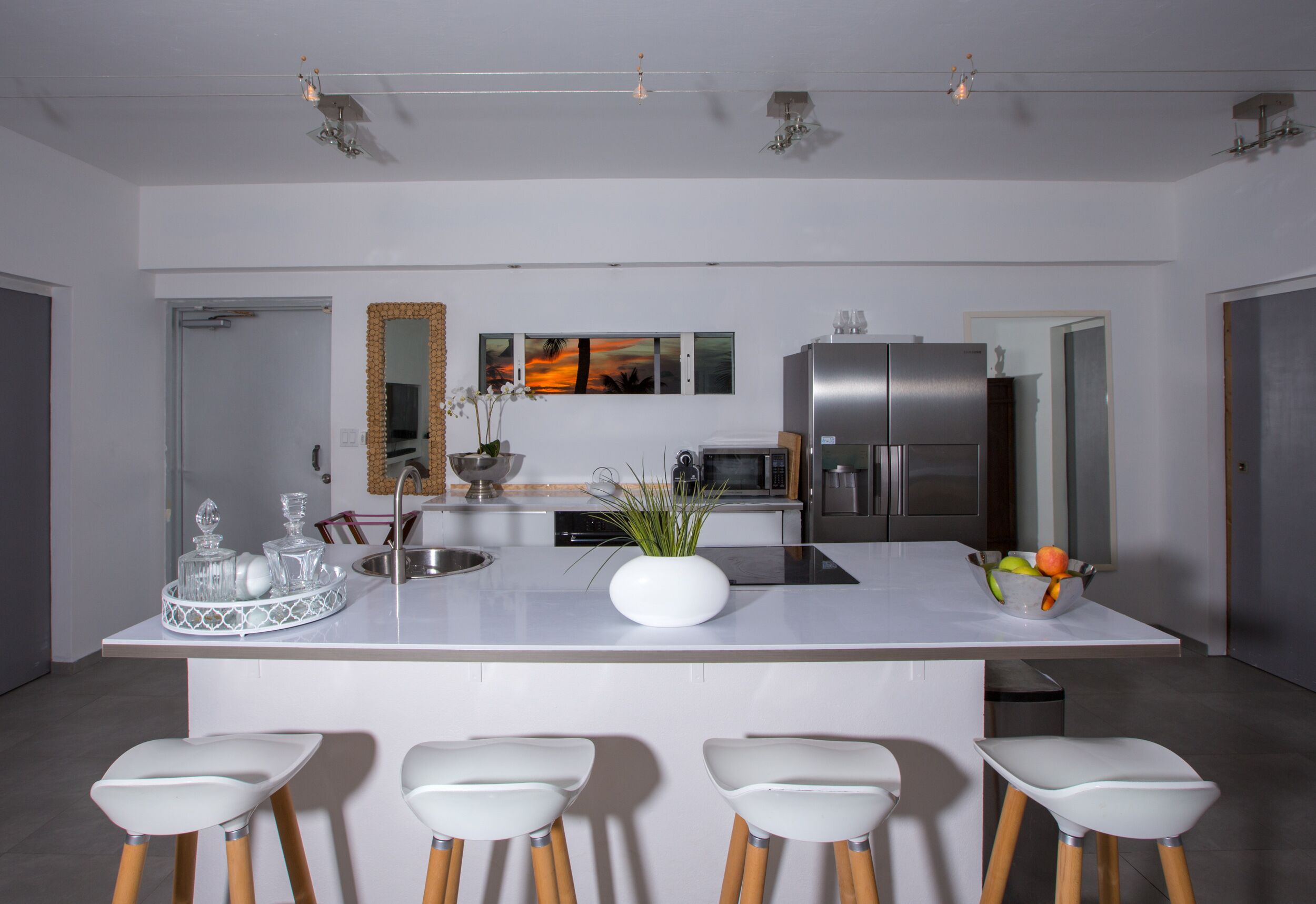 A modern kitchen with a central island, bar stools, stainless steel appliances, and a decorative mirror.