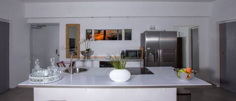 A modern kitchen with a central island, bar stools, stainless steel appliances, and a decorative mirror.