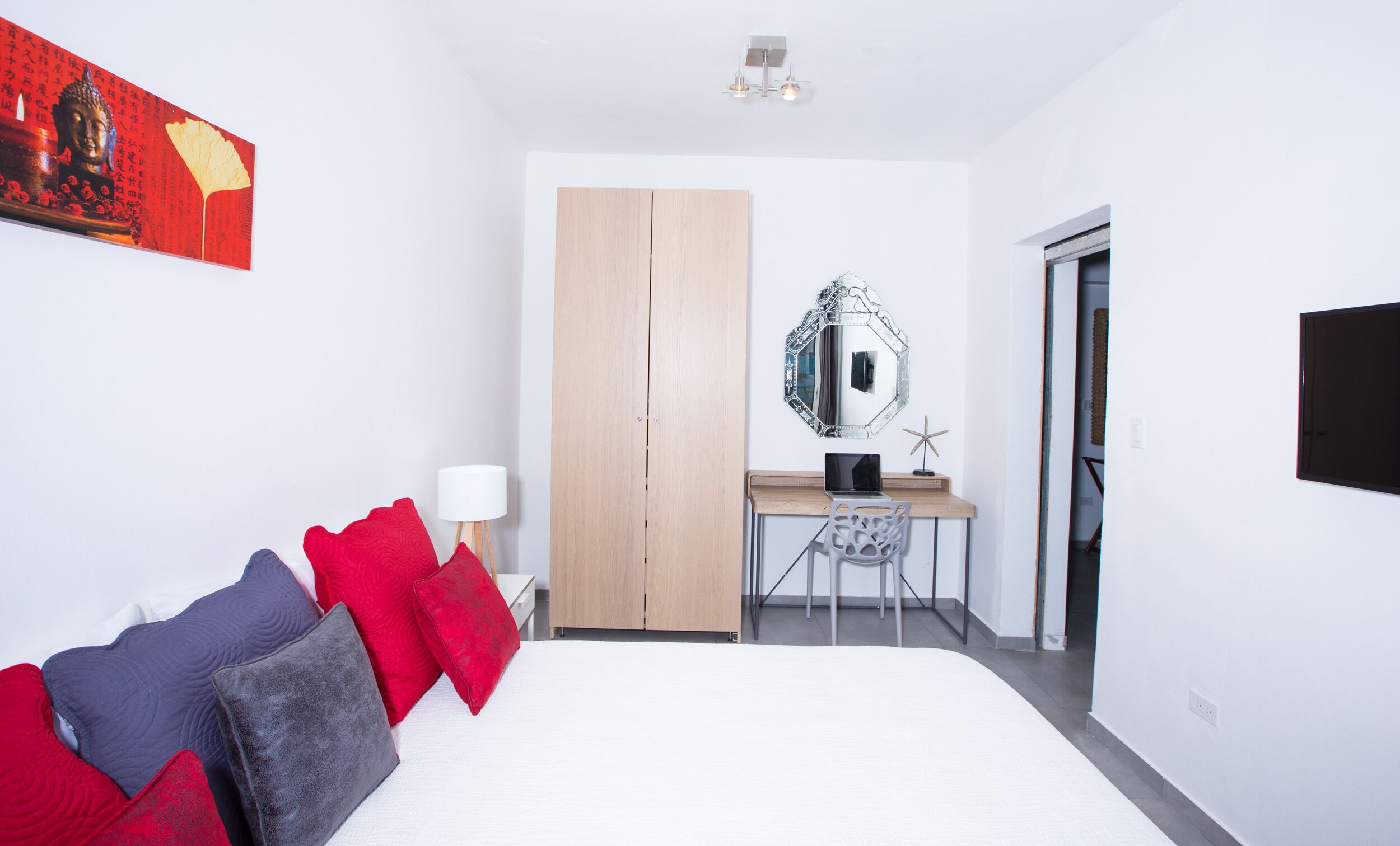 A bedroom with a bed, a desk, a chair, a wardrobe, and a mirror.