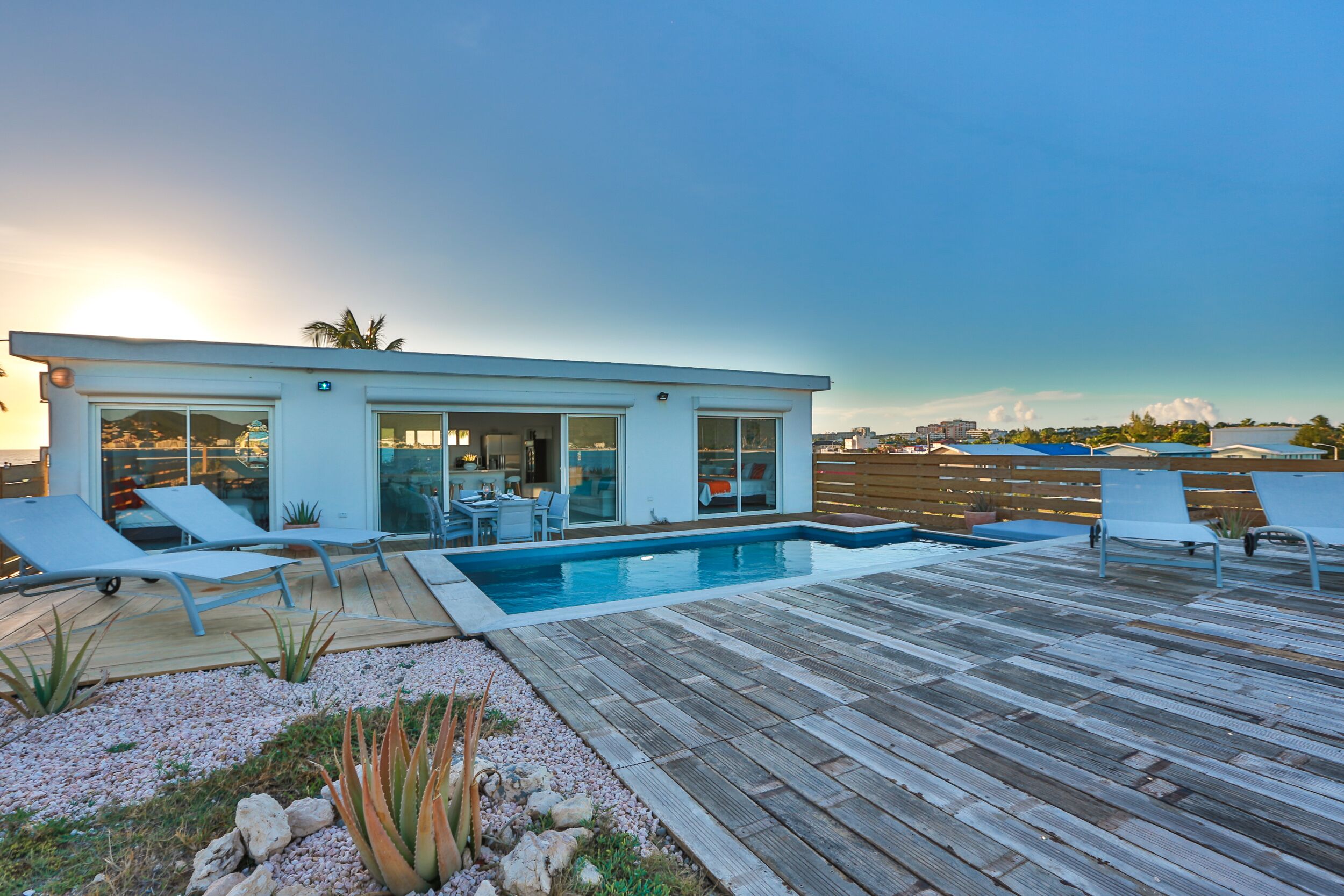 A modern house with a pool, deck chairs, and a patio area.