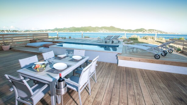 Terraza con piscina, sillas de descanso y mesa lista para comer.
