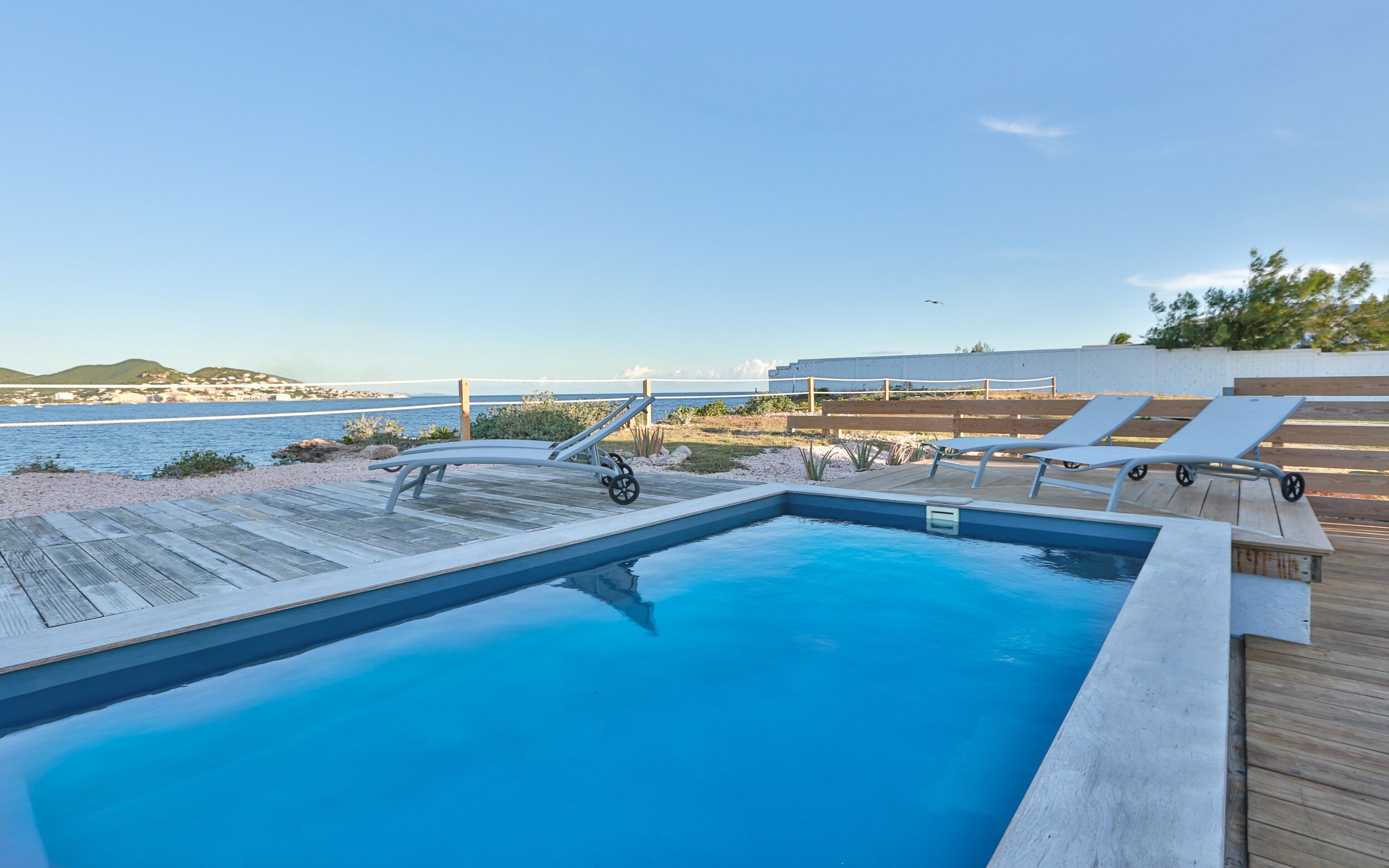 A swimming pool with lounge chairs and a wooden deck overlooking the sea.