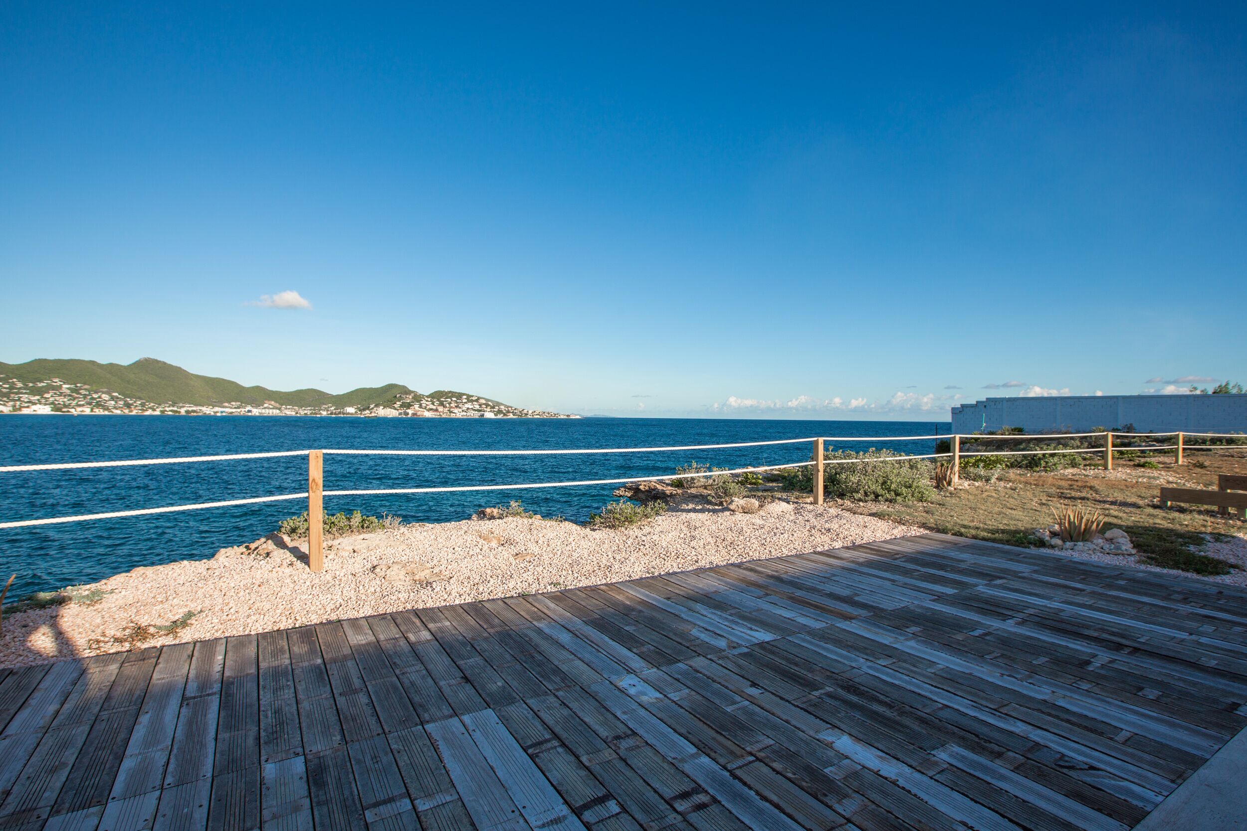 A wooden deck overlooking a beach with a clear blue sky.