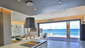A modern kitchen with a large island, a dining area with a view of the sea, and a spacious living area with a large window.