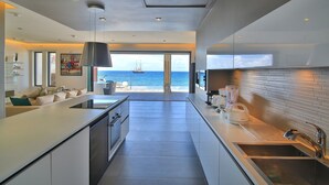 A modern kitchen with a large island, a view of the sea, and a dining area with a sofa.