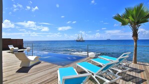 A deck with lounge chairs and a pool overlooking the sea, with a ship in the distance.
