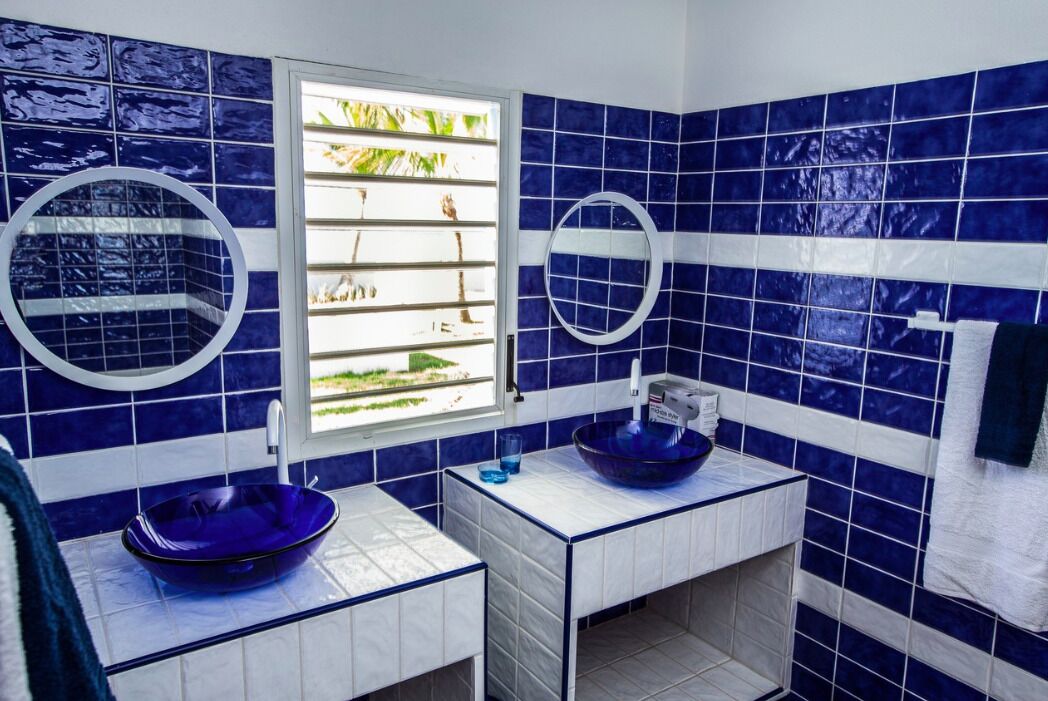 A bathroom with two sinks, blue tiles, a window, and a towel rack.