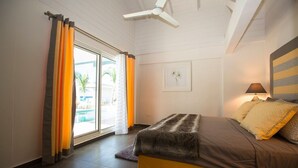 A bedroom with a bed, curtains, a ceiling fan, a window with a view, and a lamp. - Beach secrets (Simpson Bay)
