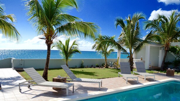 A poolside area with lounge chairs, palm trees, and a view of the ocean. - Beach secrets (Simpson Bay)