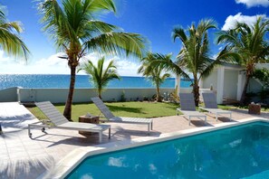Ein Poolbereich mit Liegestühlen, Palmen und Blick auf das Meer.